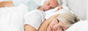 woman covering her ears while husband snores next to her