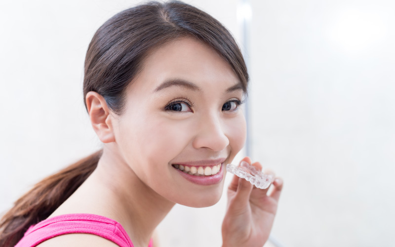 young asian woman showing clear braces versus metal braces