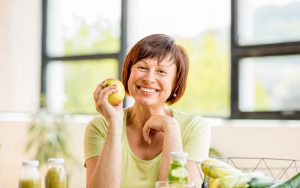 senior woman holding apple smiling showing dental implants or dentures
