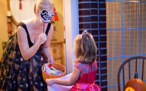 woman with mask giving out Halloween candy to young girl