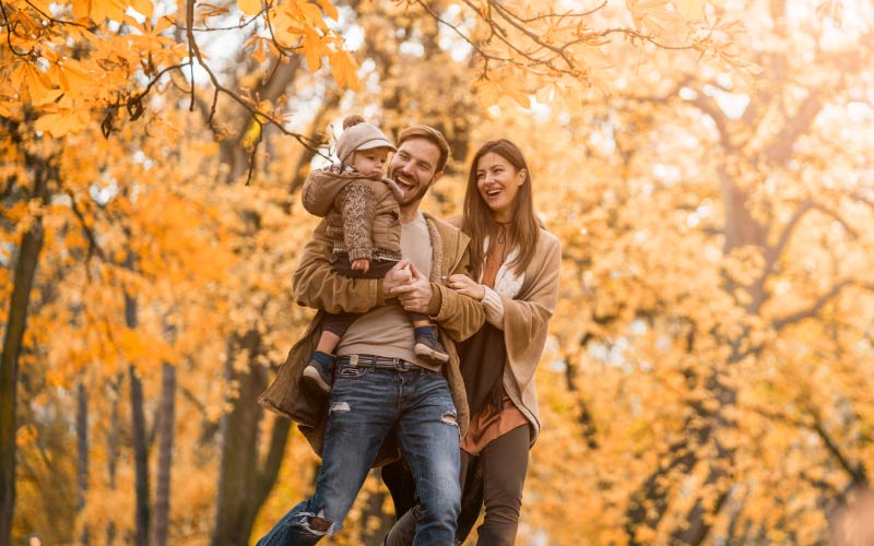 Father, mother, and child walking outside surrounded by trees with yellow leaves