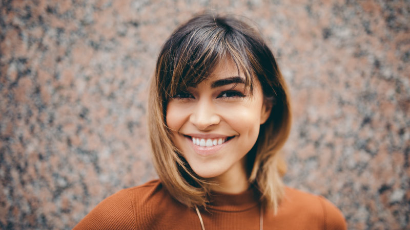 Smiling dark-haired woman wears a rust-colored blouse and necklace