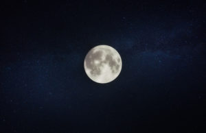 A white full moon against a navy blue midnight sky with twinkling stars during the nighttime when people sleep