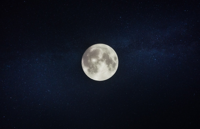 A white full moon against a navy blue midnight sky with twinkling stars during the nighttime when people sleep