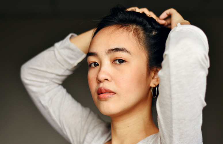 Dark-haired woman in a white sweater holds her hair back from her face, as she ponders how oral health affects skin