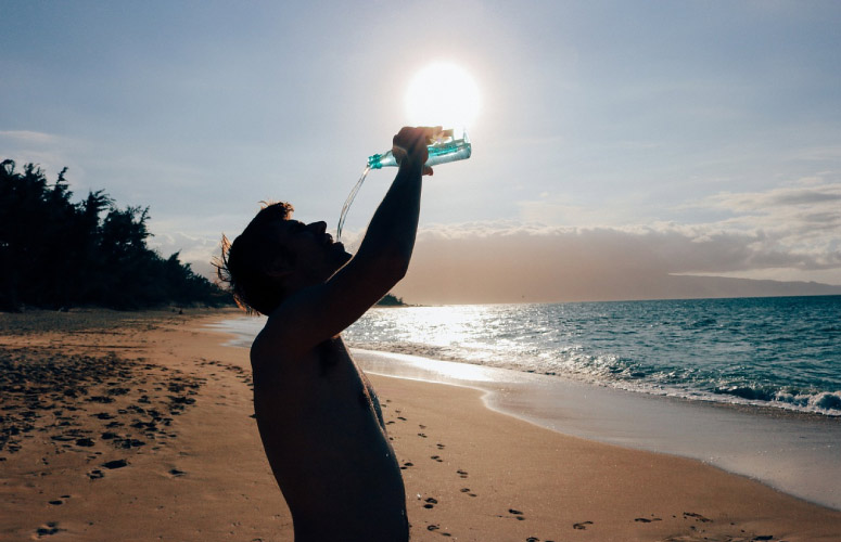 man on a beach drinking from a water bottle to prevent teeth demineralization