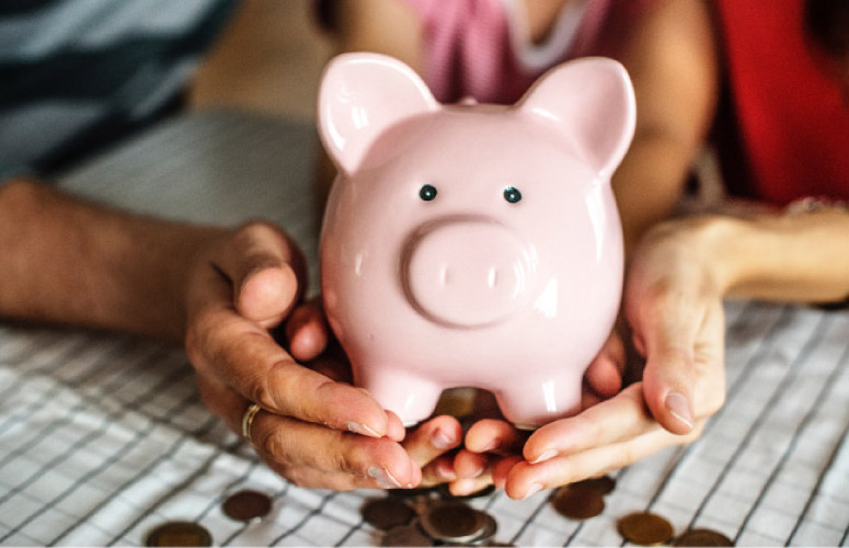 hands holding a pink piggybank with coins spilling out the bottom