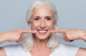 white haired woman points to her white teeth with both index fingers