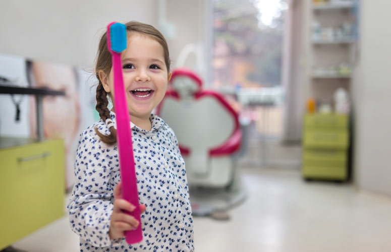 young girl laughing holding a big pink toothbrush