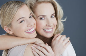 two blond women hug and smile while showng off their white teeth