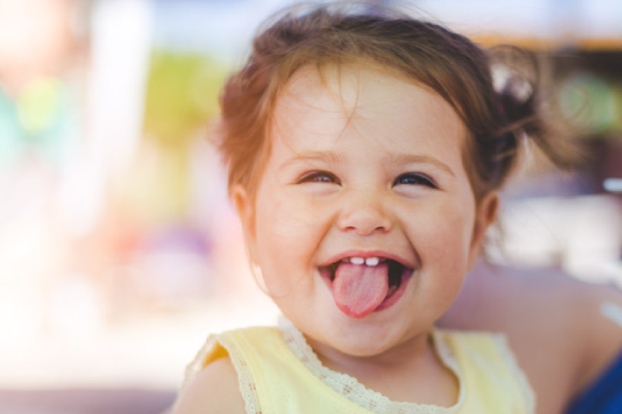 baby girl smiles and sticks out her tongue showing two baby teeth