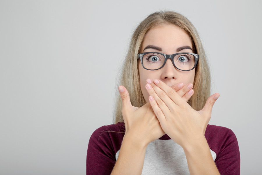 woman wearing glasses hides her mouth with both hands to cover signs of gum disease