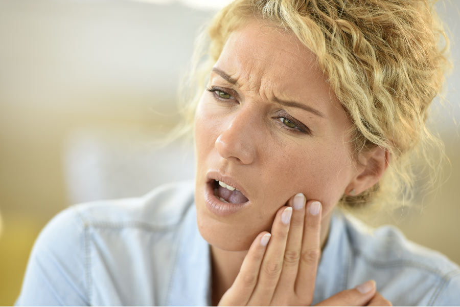 blond haired woman holds her jaw experiencing tooth sensitivity