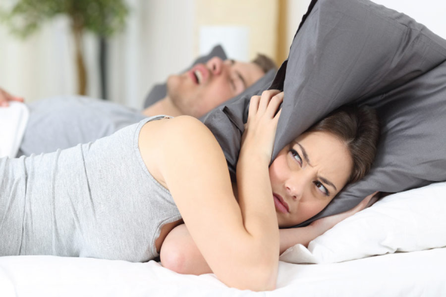 woman covers her head with a pillow to block her partners sleep apnea induced snoring
