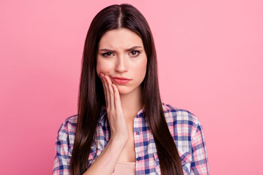 young woman holds her jaw from pain caused by sensitive teeth