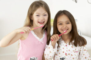 two young girls brush their teeth together.